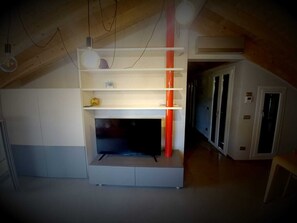 A room with a built-in entertainment unit, a white cabinet, and a red accent piece. - Attic Boutique May (Bergamo)