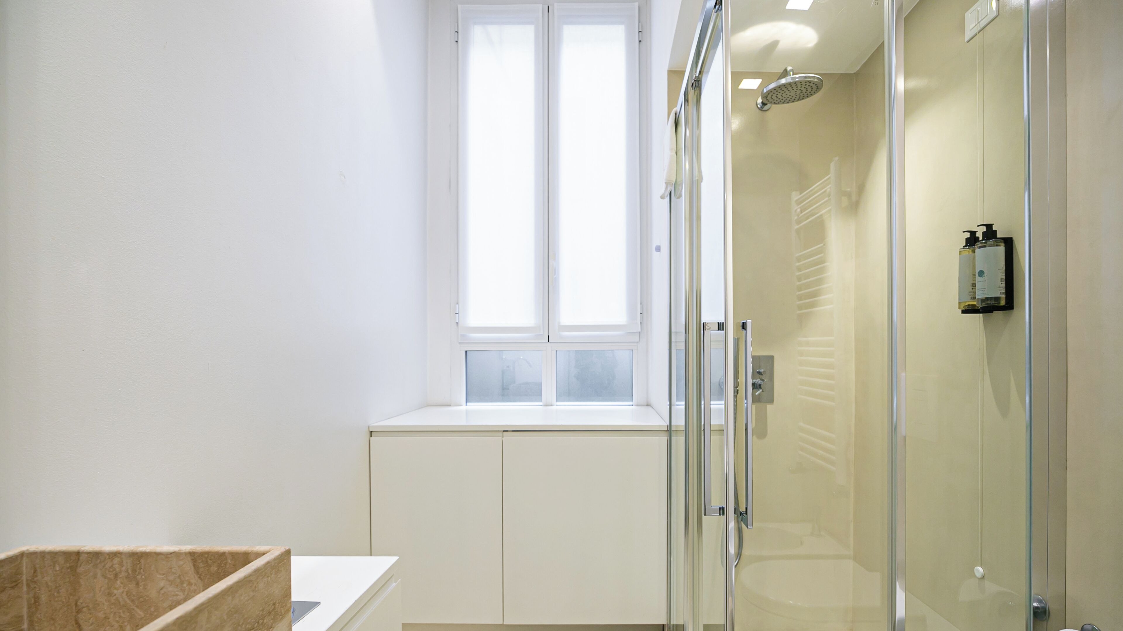 Un baño moderno con cabina de ducha de vidrio, un lavamanos blanco y una ventana sobre el lavabo.