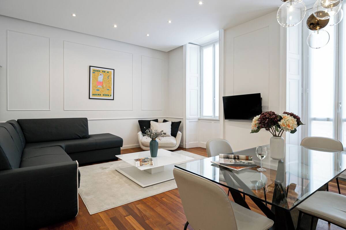 A modern living room with a black sofa, a white coffee table, and a glass dining table.