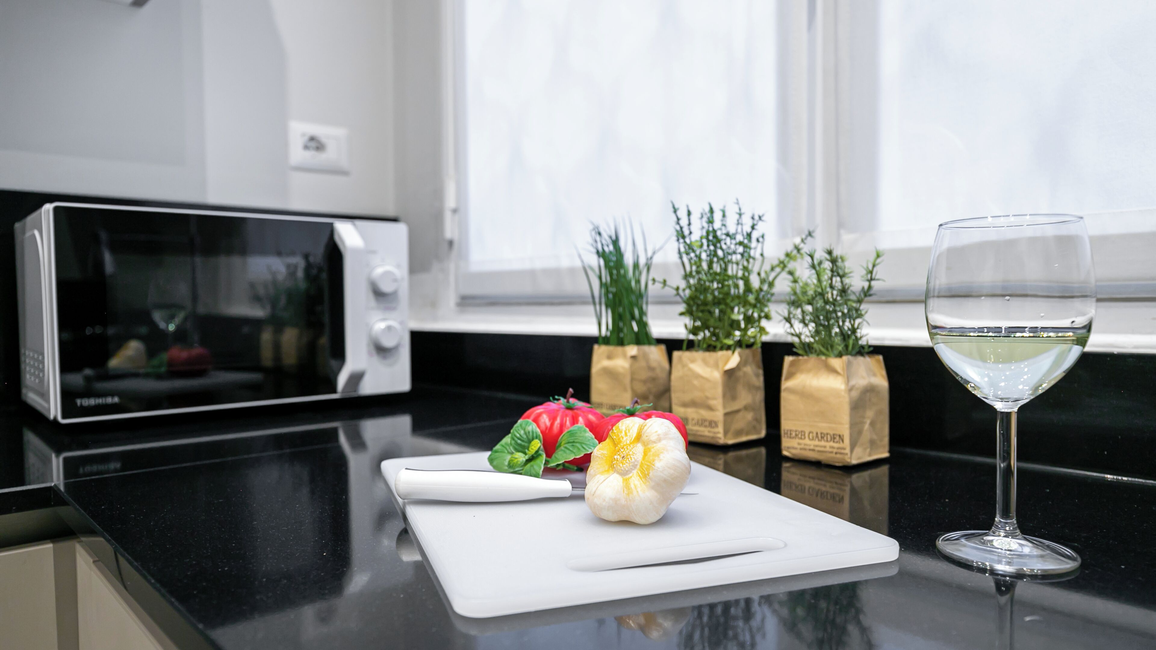Un piano di lavoro in cucina con un forno a microonde, un tagliere con verdure e un bicchiere da vino.