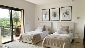 A bedroom with two beds, a large window with a view, and framed botanical prints on the wall.