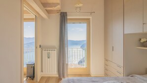 Quarto com teto de madeira, cama com roupa de cama estampada, radiador e vista para o mar através de uma janela.