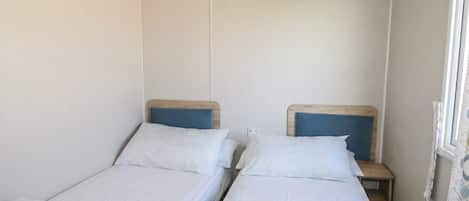 Ein Zimmer mit zwei Einzelbetten, Holz-Kopfteilen, weißer Bettwäsche und einem Fenster mit Vorhang.