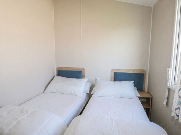A room with two single beds, wooden headboards, white bedding, and a window with a curtain.