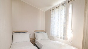 Quarto duplo com duas camas individuais, uma pequena mesa de cabeceira e uma janela com cortinas estampadas.