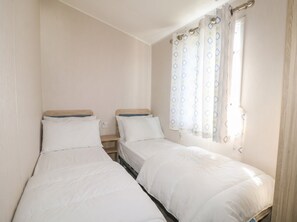 A twin room with two single beds, a small bedside table, and a window with patterned curtains.