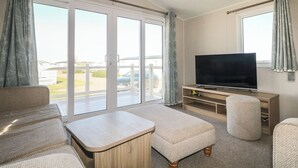 Uma sala de estar com sofá, pufê, televisão e uma porta de vidro deslizante que dá para uma varanda.