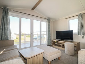 A living room with a sofa, ottoman, TV, and a sliding glass door leading to a balcony.