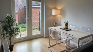 Un comedor moderno con una mesa blanca, sillas transparentes, una lámpara y una planta en maceta.
