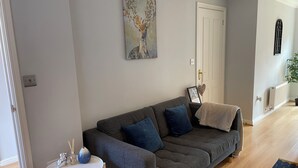 Un salón con un sofá gris, una mesita blanca y un cuadro en la pared.
