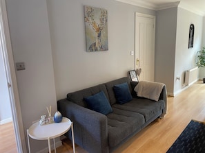 Ein Wohnzimmer mit grauem Sofa, einem kleinen weißen Tisch und einem Bild an der Wand.