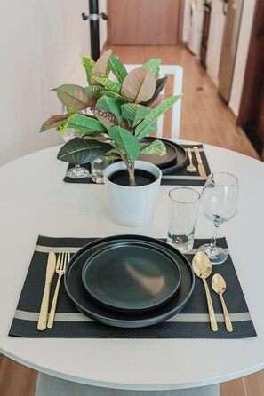 A dining table set with black plates, gold cutlery, and a potted plant. - PVH - Al Jawhara - Charming Studio (Dubai)