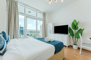 A hotel room with a large bed, a TV, a potted plant, and a view of the city. - PVH - Al Jawhara - Charming Studio (Dubai)