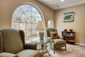 A room with large arched windows, a glass coffee table, two green upholstered chairs, a lamp, a bookshelf, and a wall-mounted bear illustration. - Close to Ober Gatlinburg, 3 stories, 3 king size beds, hot tub, pool table (Gatlinburg)