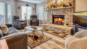 A living room with a stone fireplace, leather chairs, a glass coffee table, and a television. - Amazing Gatlinburg Views - Briarcliff Subdivision, Hot Tub, Game Room, Sleeps 8 (Gatlinburg)
