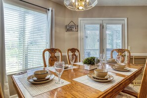 A dining room with a wooden table set for four, two chairs, a chandelier, and a window with blinds. - Close to Ober Gatlinburg, 3 stories, 3 king size beds, hot tub, pool table (Gatlinburg)