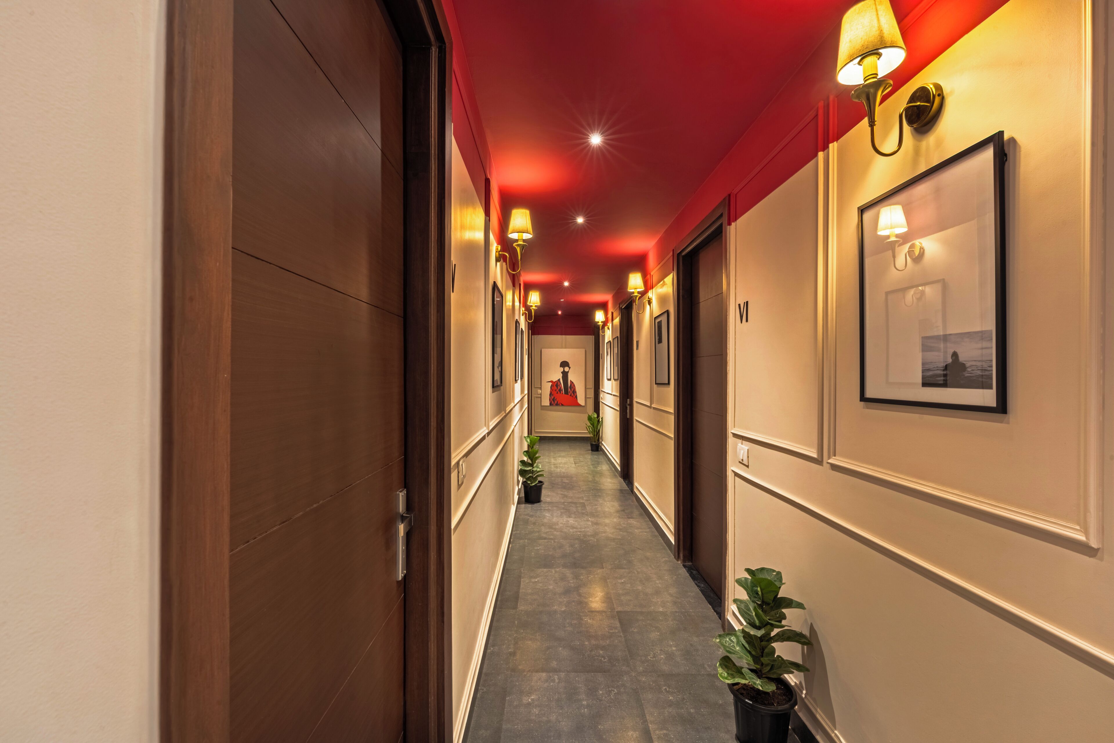 A hotel hallway with wooden doors, framed pictures, and potted plants.