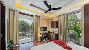 Habitación de hotel con cama, escritorio, televisión, balcón con cortinas y ventilador de techo.