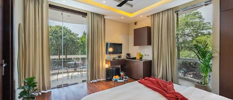 A hotel room with a bed, a desk, a TV, a balcony with curtains, and a ceiling fan.