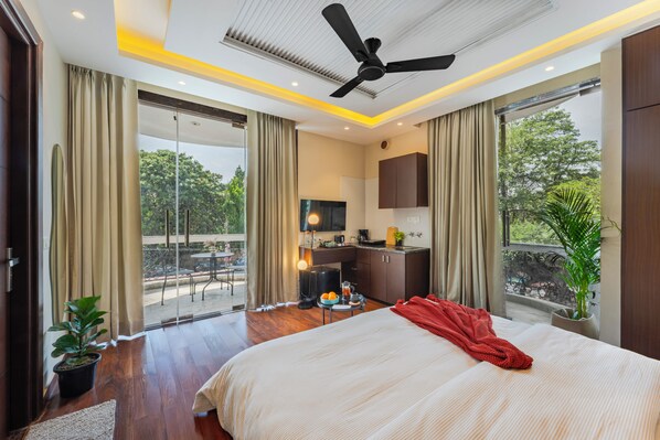 Habitación de hotel con cama, escritorio, televisión, balcón con cortinas y ventilador de techo.