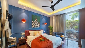 Un dormitorio moderno con una cama grande, un ventilador de techo, una mesita de noche, una silla, una ventana con vistas y una pared decorada con un cuadro.