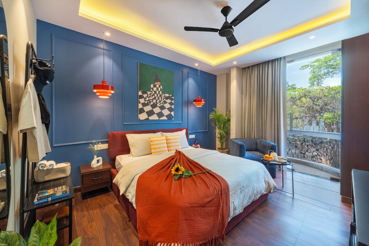 Um quarto moderno com uma cama grande, um ventilador de teto, uma mesinha de cabeceira, uma cadeira, uma janela com vista e uma parede com um quadro.