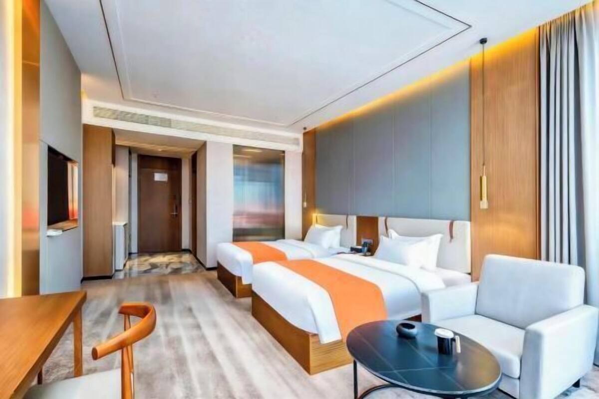 A hotel room with two beds, a sofa, a dining table, and a TV.