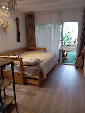 Ein Schlafzimmer mit einem hölzernen Bett, einem Schreibtisch und Blick auf einen Garten durch eine Schiebetür.