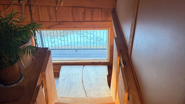 A wooden staircase leading to a balcony with a metal railing, a potted plant, and a wooden ceiling with a decorative element.