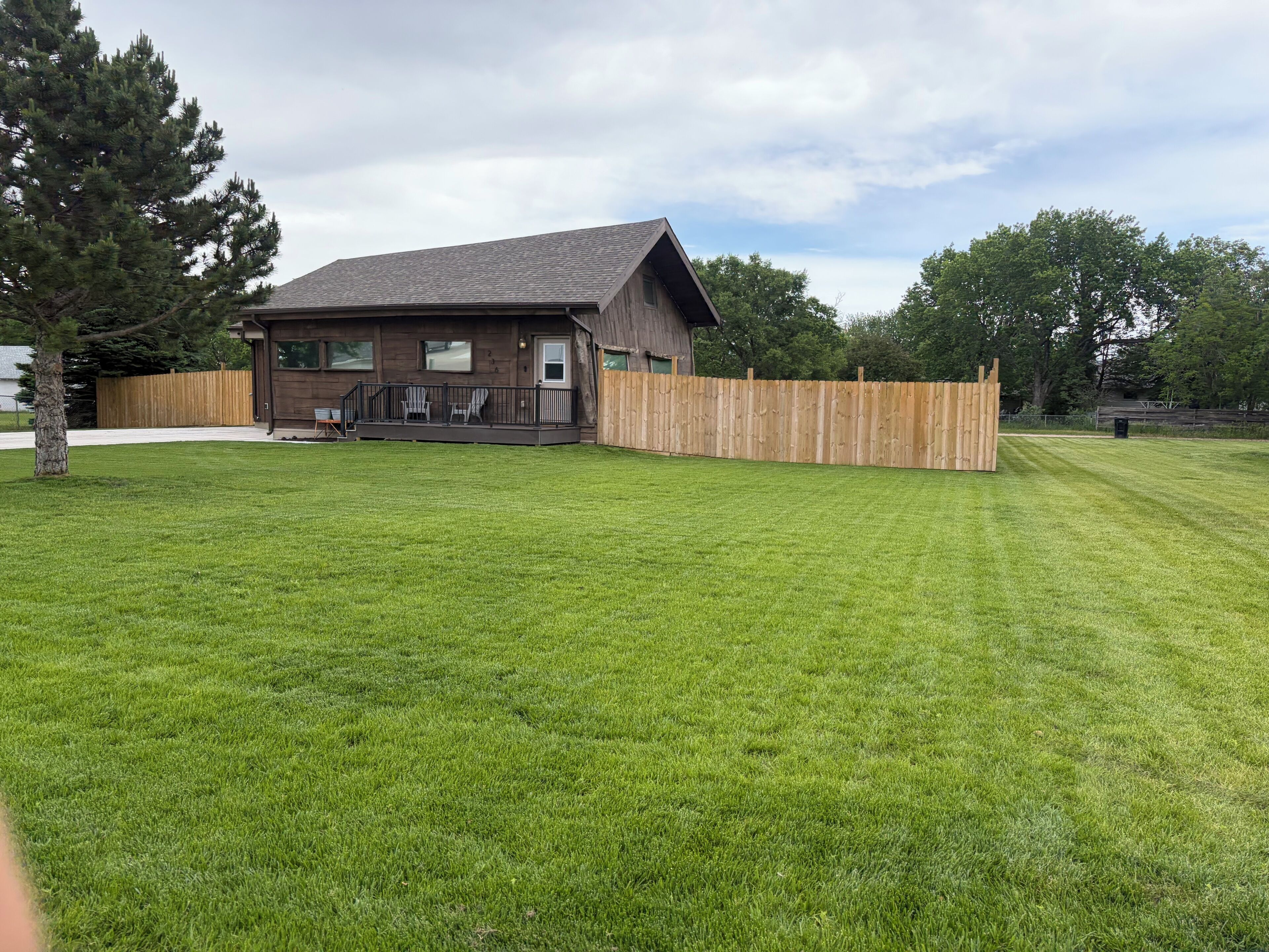 A house with a fenced backyard, a porch with chairs, and a wooden deck.