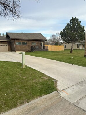 A residential property with a garage, a wooden deck, a lawn, and a large tree.