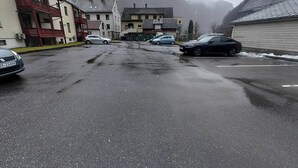 En gata med parkerade bilar, byggnader och ett berg i bakgrunden.