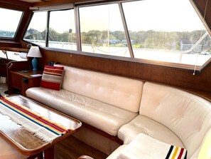 A cabin with a leather sofa, a table with a lamp, and large windows offering a view of the water and greenery.