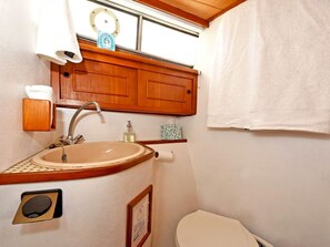 A compact bathroom with a sink, toilet, and wooden cabinet.
