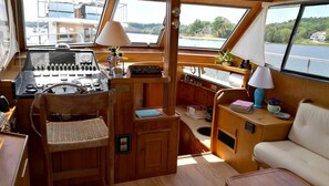 A compact boat interior with a wooden dashboard, steering wheel, and a small seating area with a cushioned bench. - Experience the Magic of Sleeping Your Own Private Yacht in Damariscotta, Maine (Damariscotta)