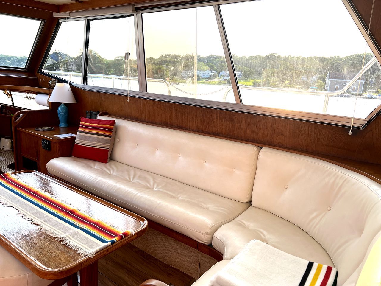A cabin with a leather sofa, a table with a lamp, and large windows offering a view of the water and greenery.