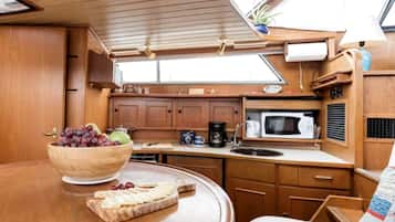 A compact kitchen with wooden cabinets, a microwave, a sink, and a dining area with a bowl of fruit and cheese.