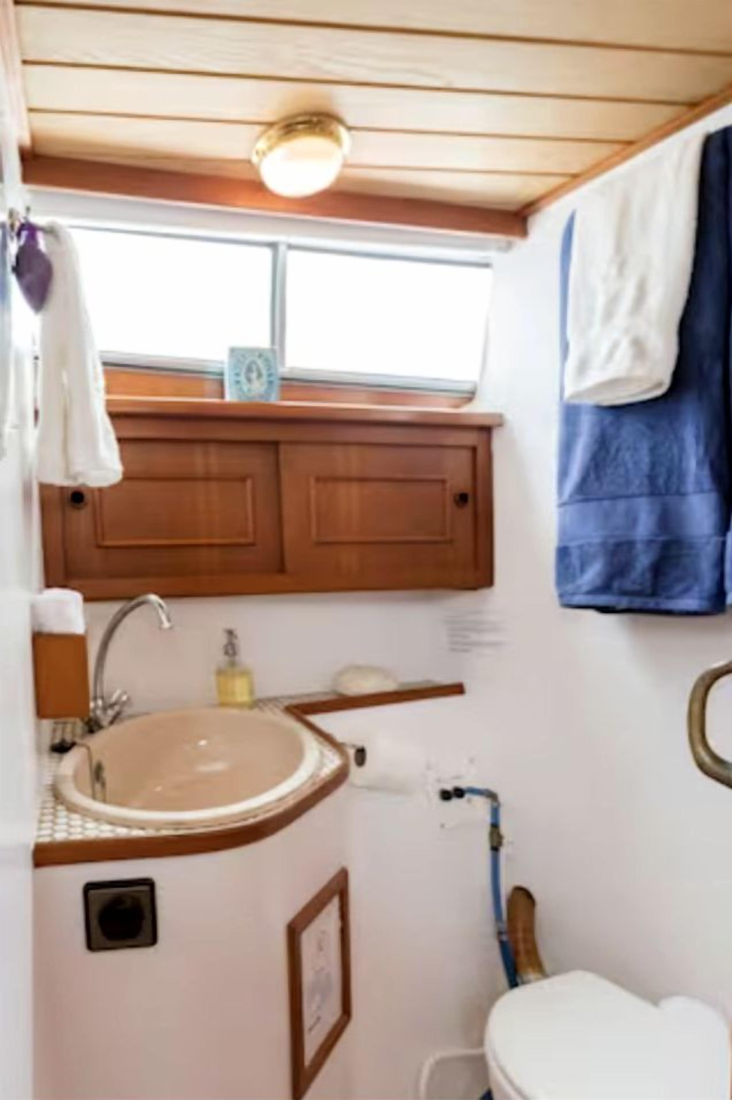 A compact bathroom with a wooden vanity, a sink, a toilet, and a window above the vanity.
