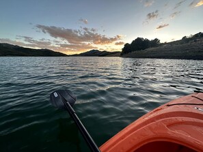 Un kayak sur une étendue d’eau calme, avec une pagaie, entouré d’un paysage naturel.