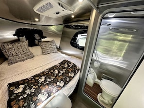 Un intérieur de camping-car compact comprenant un lit, une petite salle de bain et un coin cuisine.