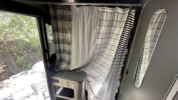 A van interior with a striped curtain, a small stool, and a window with a view of trees.