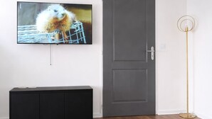 Een kamer met een donkergrijze deur, een zwarte entertainmentkast en een vloerlamp.