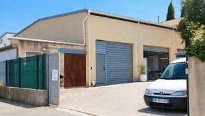 Een gebouw met een garagepoort, een witte auto ervoor geparkeerd, en een groene omheining.