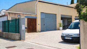 Un bâtiment avec une porte de garage, une voiture blanche garée devant et une clôture verte.