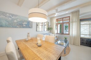 Een eetruimte met een houten tafel, stoelen, een hangende lamp en een groot abstract schilderij aan de muur.