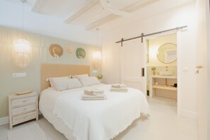 Ein Schlafzimmer mit Bett, Nachttischen, Kommode, Spiegel und einem Badezimmer mit Waschbecken und Toilette.