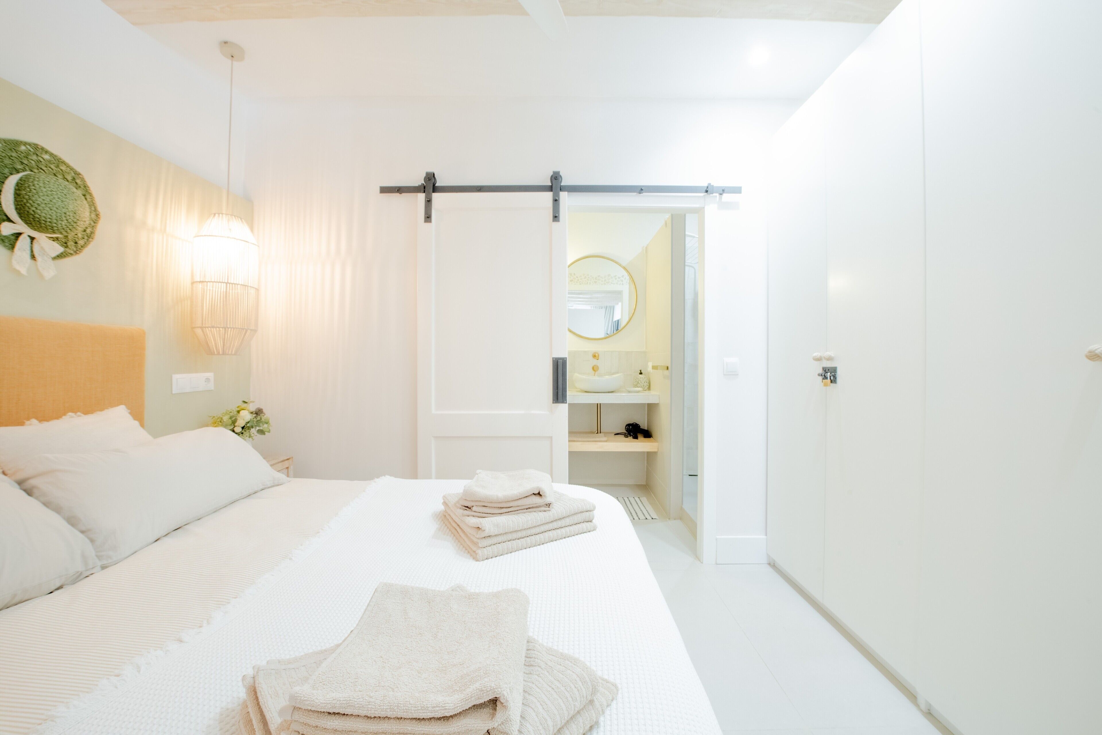 Une chambre d’hôtel comprenant un lit, une table de chevet avec une lampe, une porte coulissante donnant accès à la salle de bain et un miroir fixé au mur.
