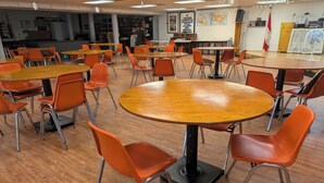 Un aula con mesas redondas y sillas naranja, suelo de madera y carteles educativos en las paredes.