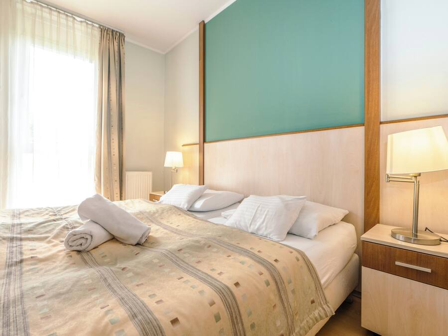 Cama bem arrumada com colcha estampada, luminária de cabeceira e mesa de apoio.