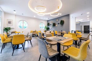 A modern dining area with round tables and chairs, recessed ceiling lighting, and a view of the outdoors through large windows. - PRIME STAY BUDAPEST (Budapest)